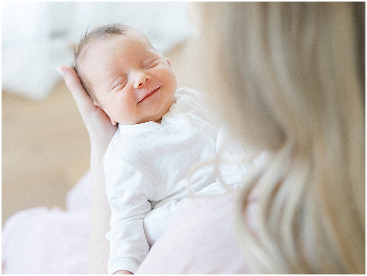 smiling newborn baby in mother’s arms during newborn photo shoot