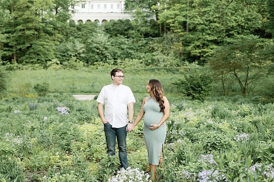 pregnant wife with husband smiling in a field at 100 acre woods in indianapolis