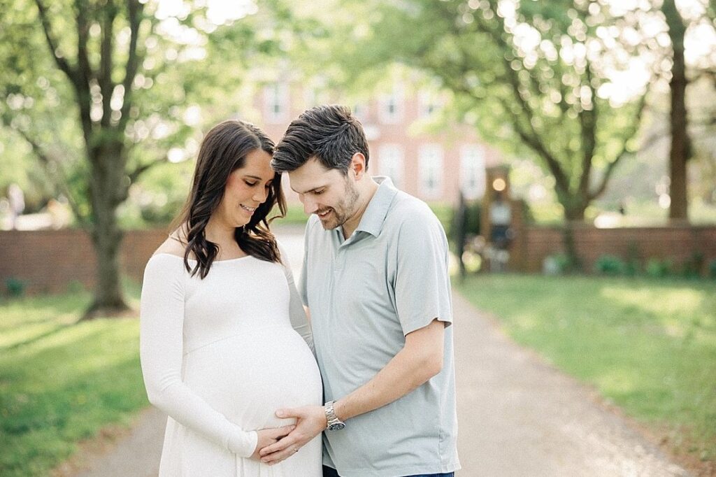 pregnant woman and husband smiling at woman’s stomach at coxhall gardens in carmel, indiana