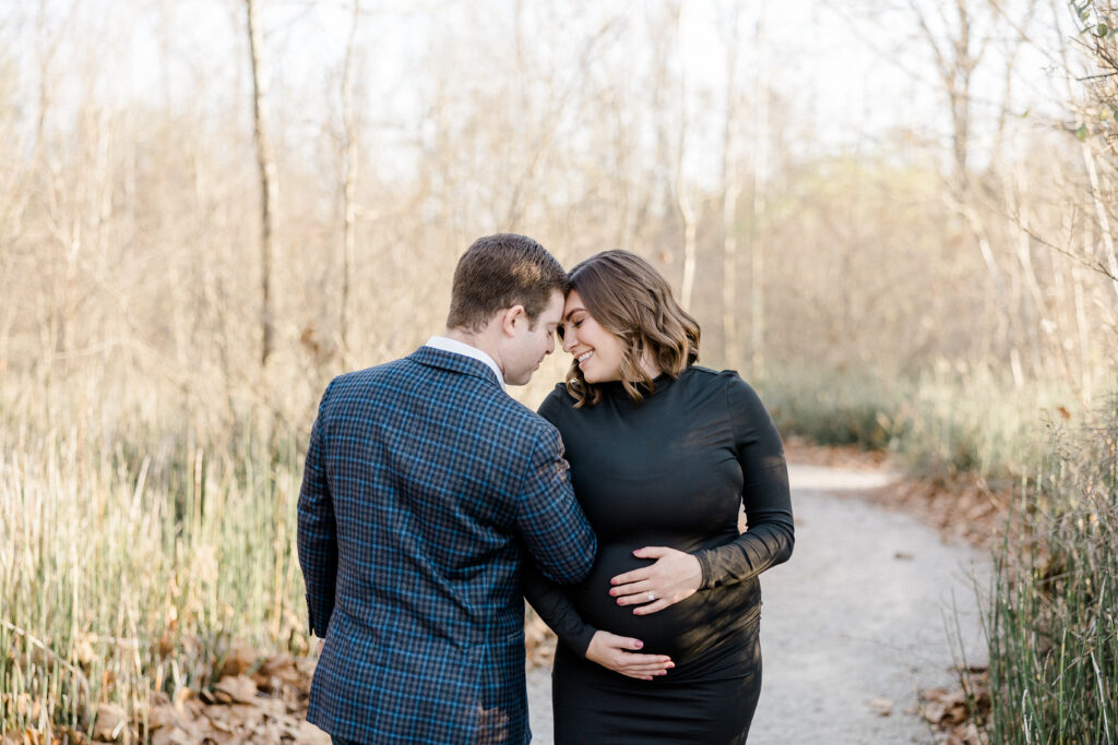 woman and man holding each other during maternity photo shoot at founders park in carmel, indiana