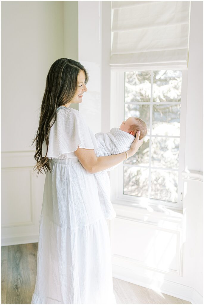 Mother holds newborn in all white studio session