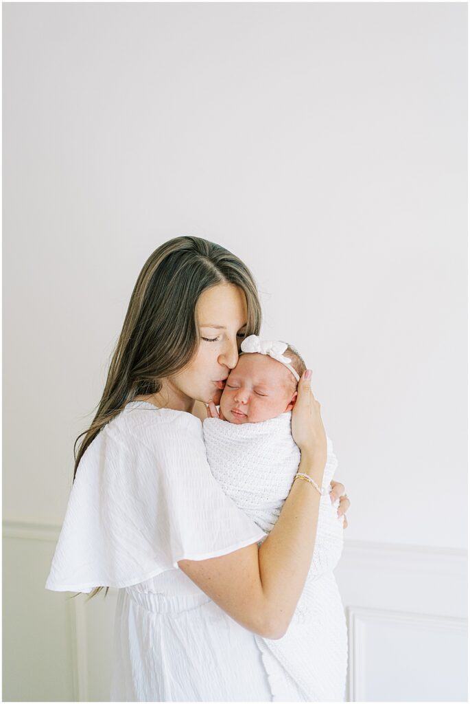Mother holds newborn in all white studio session