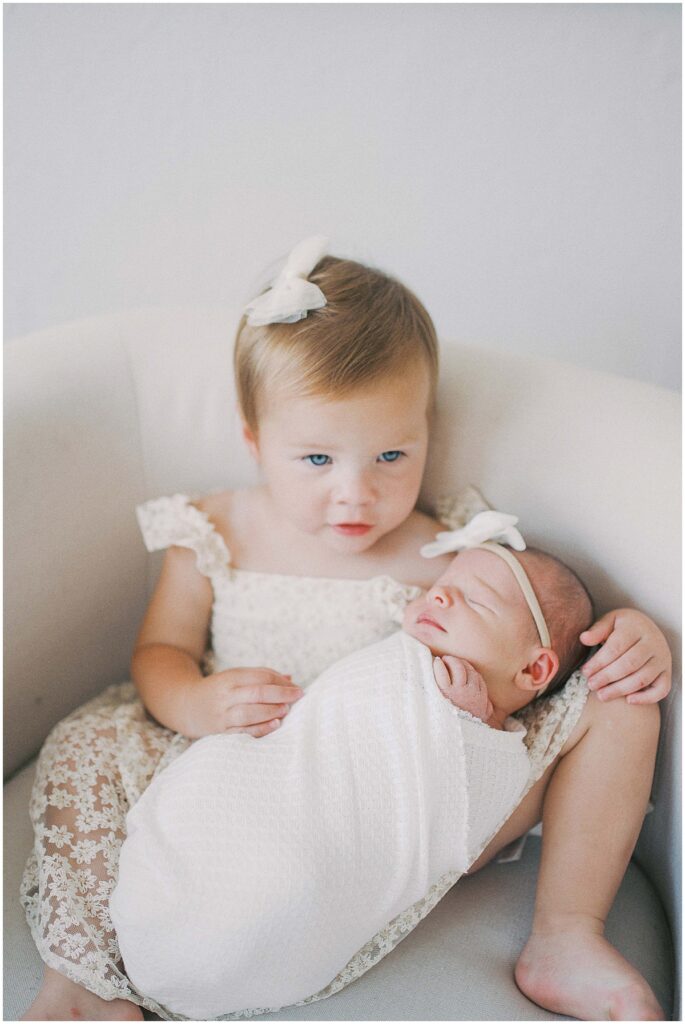 Sister in cream floral dress holds newborn during Indianapolis studio session
