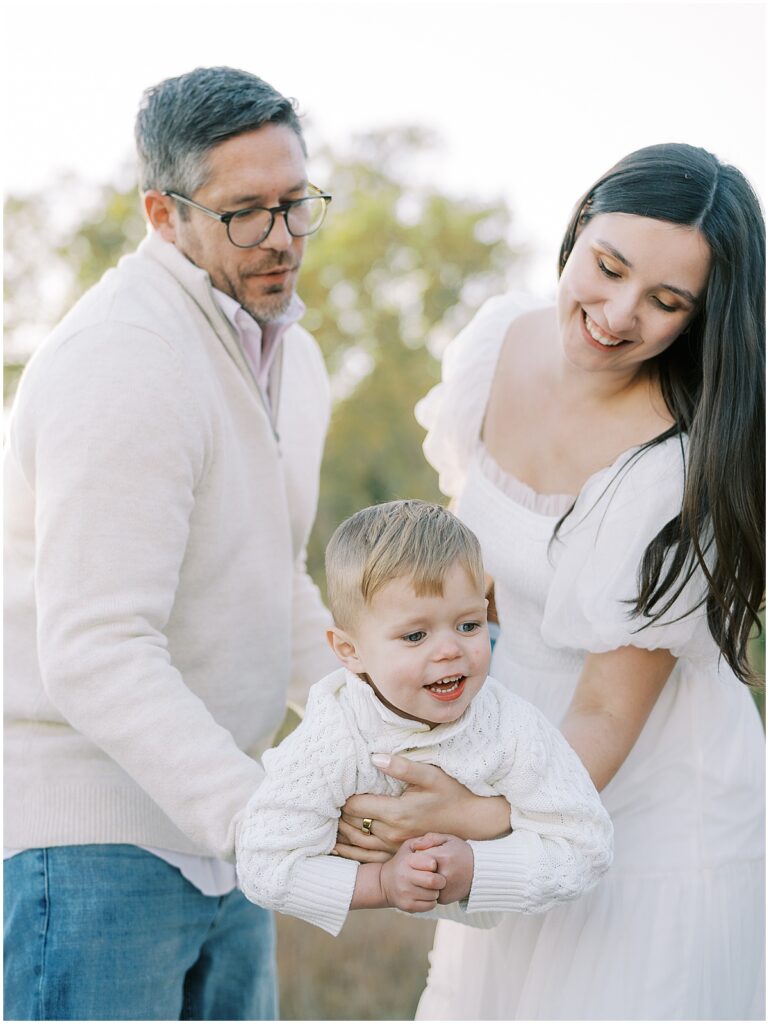 Parents carry son in white sweater during Carmel Indiana fall family photos