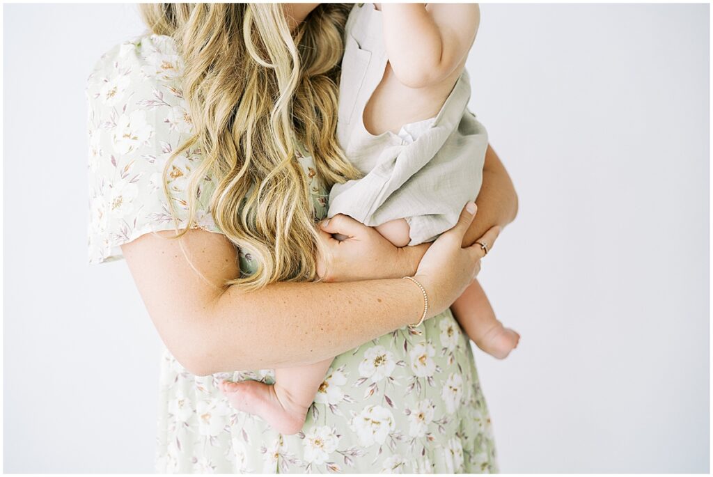 Mom in light green floral dress hugs child during cake smash photo session