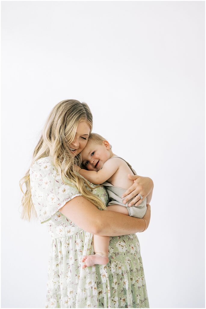 Mom in light green floral dress hugs child during cake smash photo