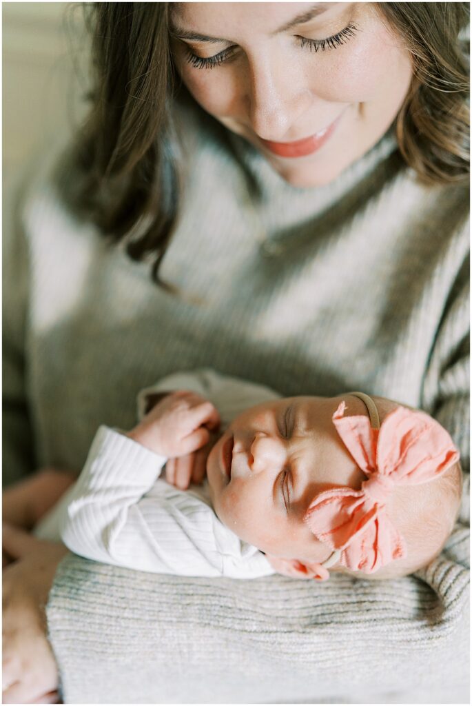 Mom holds baby with pink bow during newborn photo session