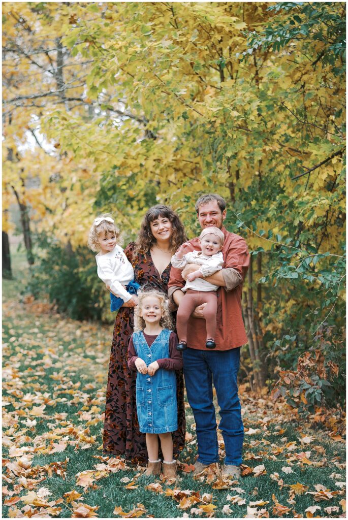 Parents with three daughters in front of fall leaves during at home photo session