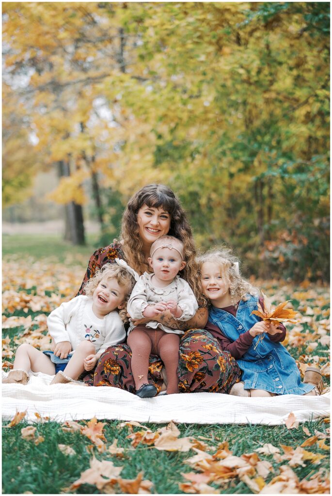 Mother and daughters surrounded by fall leaves during at home photo session