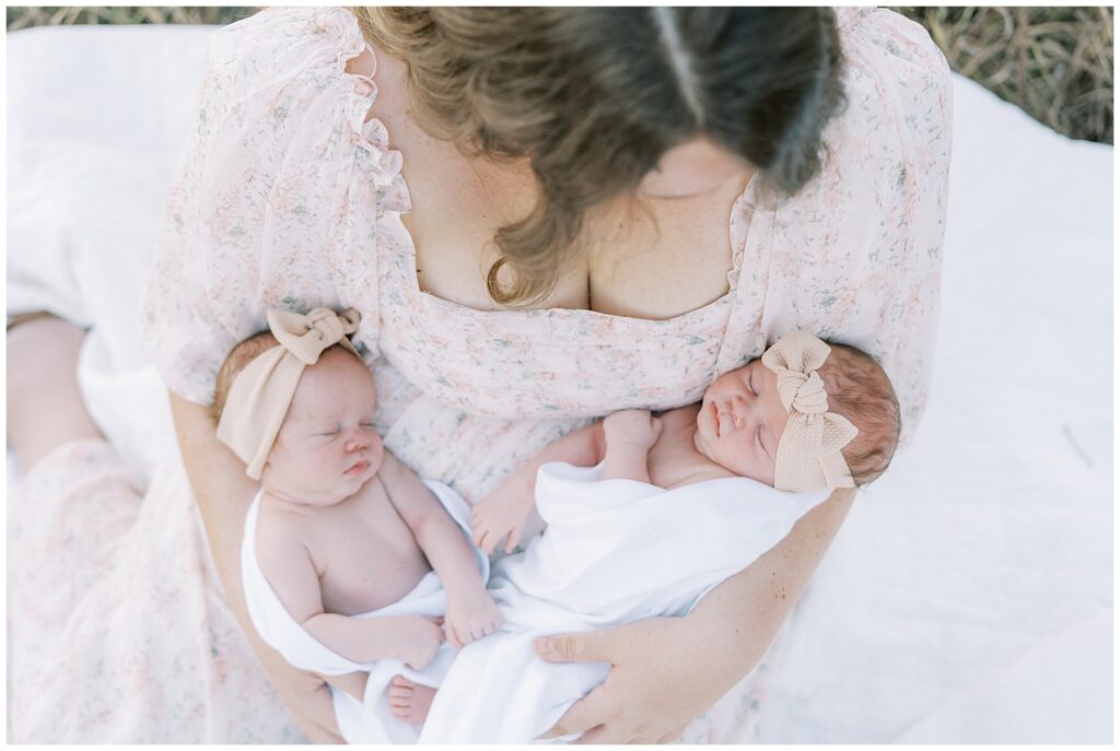 Mother in light pink holds twin newborn daughters during Carmel Indiana photo session