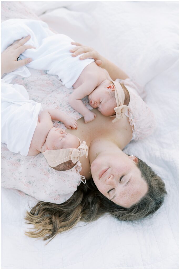 Mother in light pink holds twin newborn daughters during Carmel Indiana photo session